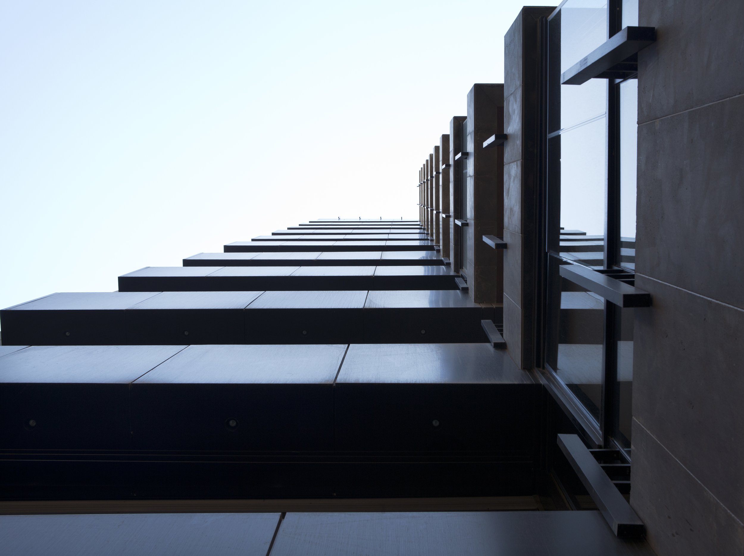 Low-angle view of a modern tall building with black window frames and beige exterior wall, taken from the ground looking upward toward the sky.