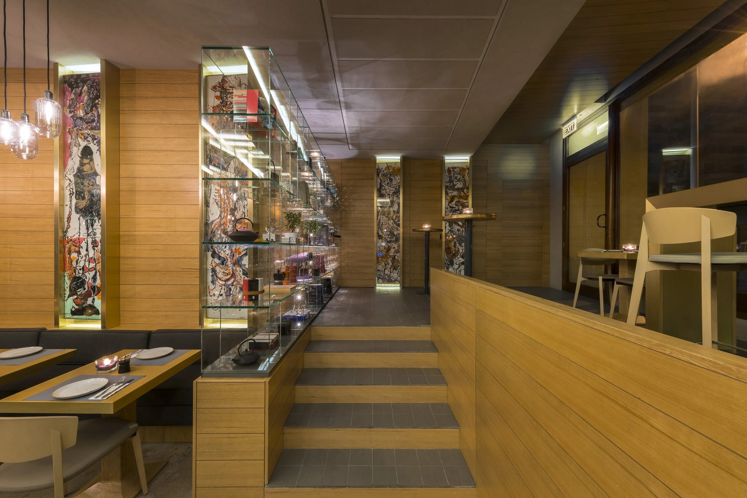 Interior of a restaurant with wooden paneling, glass display case, tables set for dining, and decorative artwork on the walls.