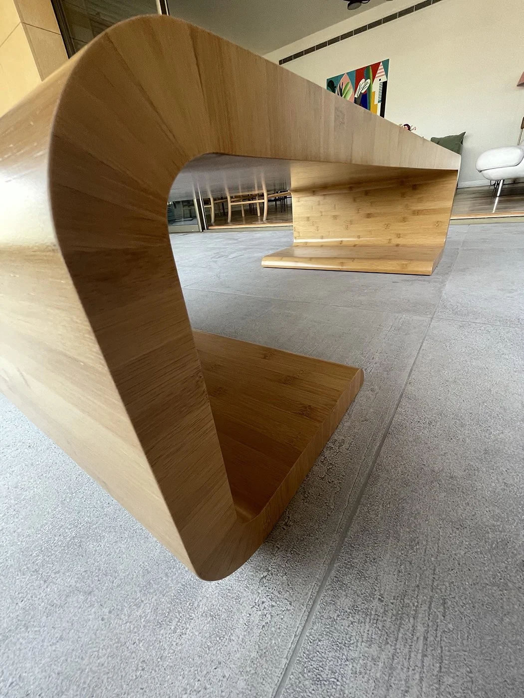 Close-up of a modern wooden bench with a curved design, placed on a tiled floor in a contemporary living space.