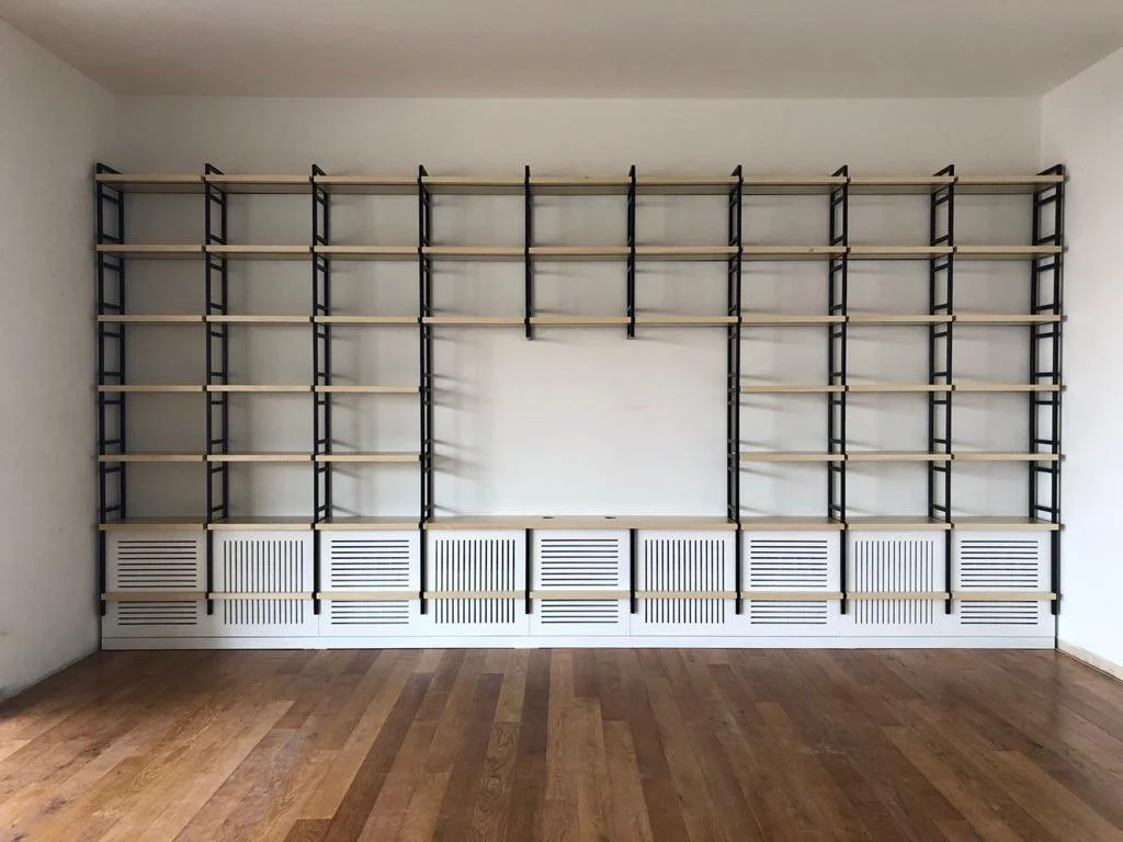 Empty black and beige shelving unit in a room with hardwood floor and white walls.