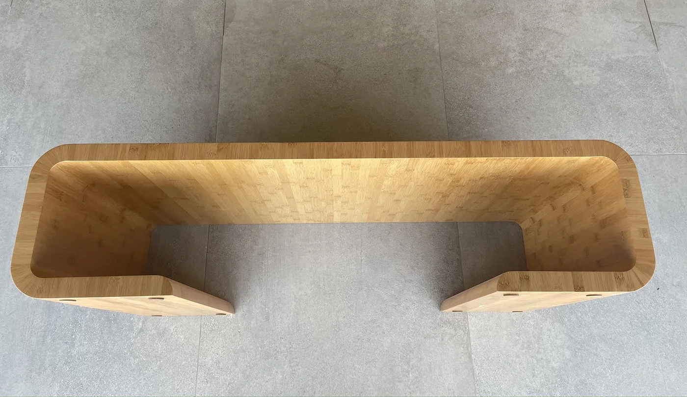 A top view of a modern wooden bench with a curved rectangular shape, placed on a tiled floor.