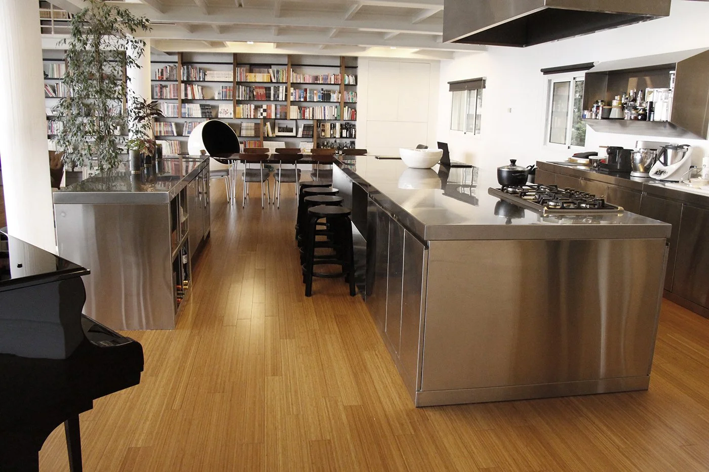 Modern kitchen with stainless steel island, black bar stools, and a bookshelf wall in the background.