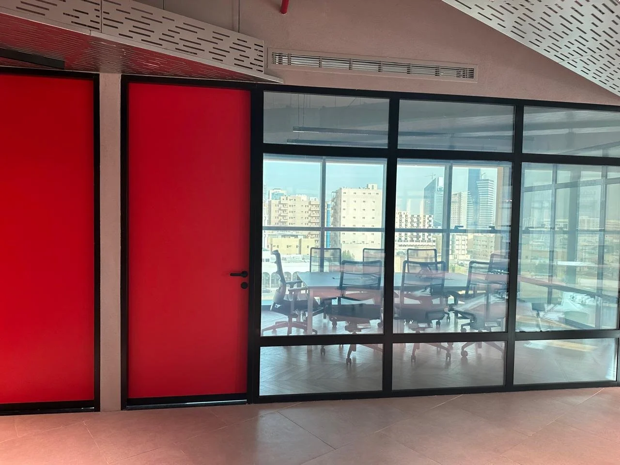 Modern office conference room with glass walls, displaying city skyline view, and red-colored doors.