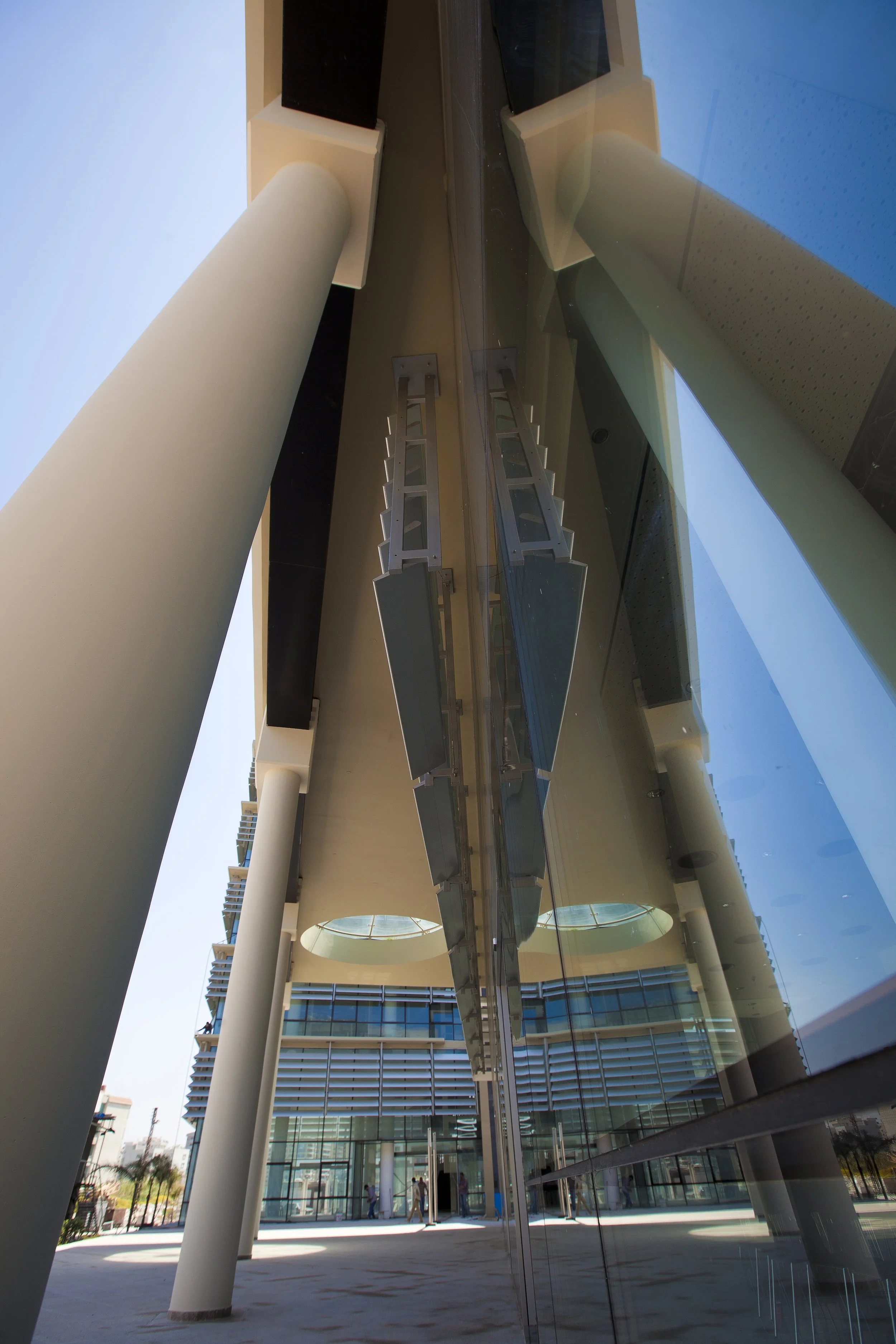 Modern building with large glass windows, white cylindrical columns, and a walkway at the entrance with people inside.