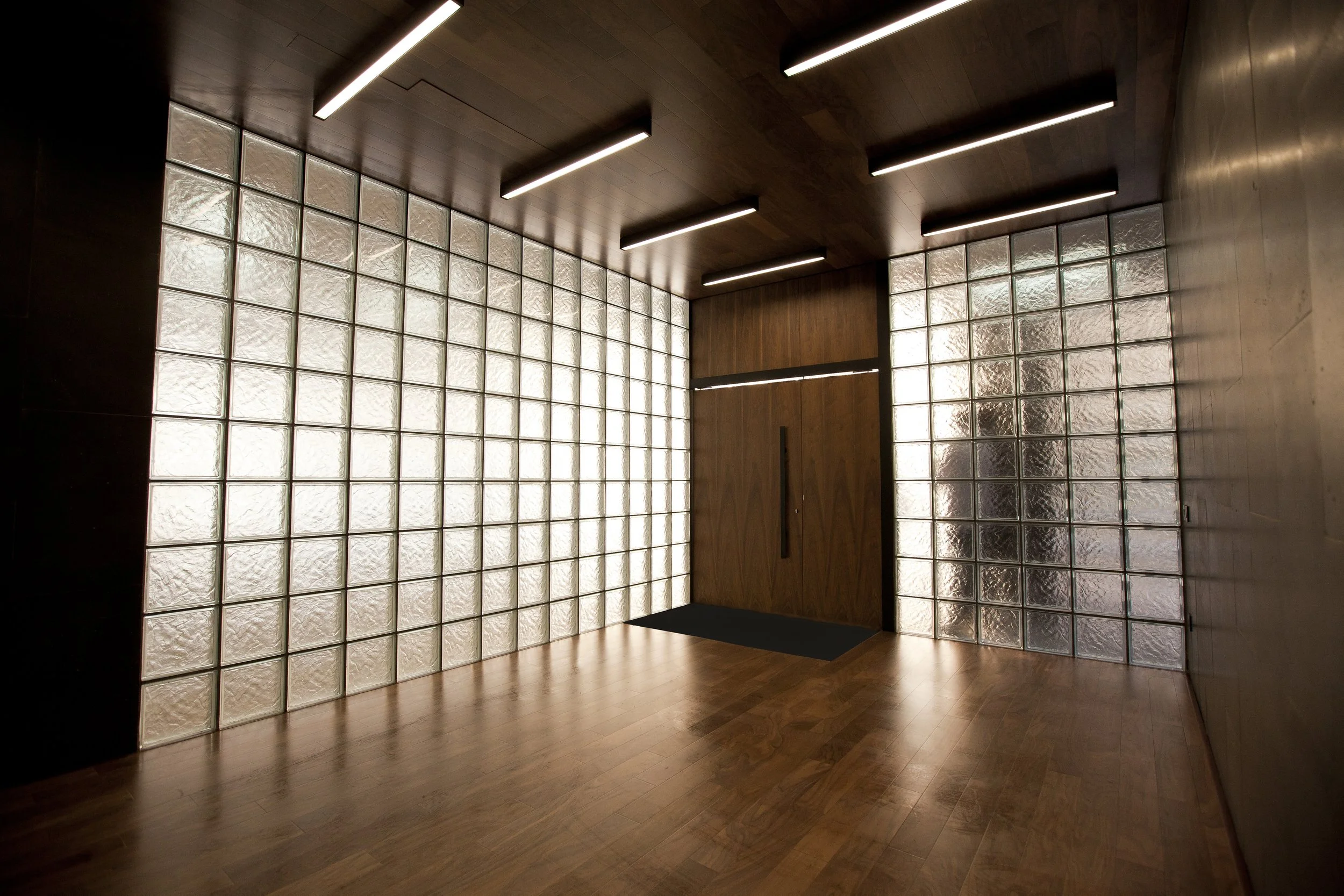 Empty modern room with wooden floors, wooden ceiling, glass block walls, and a wooden door in the center.