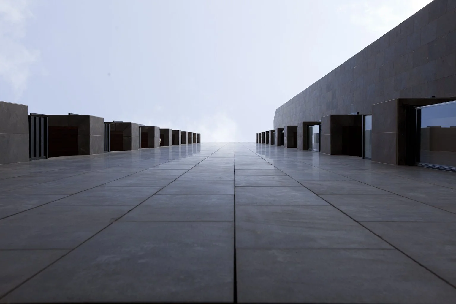 Low-angle view of modern building with rectangular windows and dark stone exterior, against a cloudy sky.