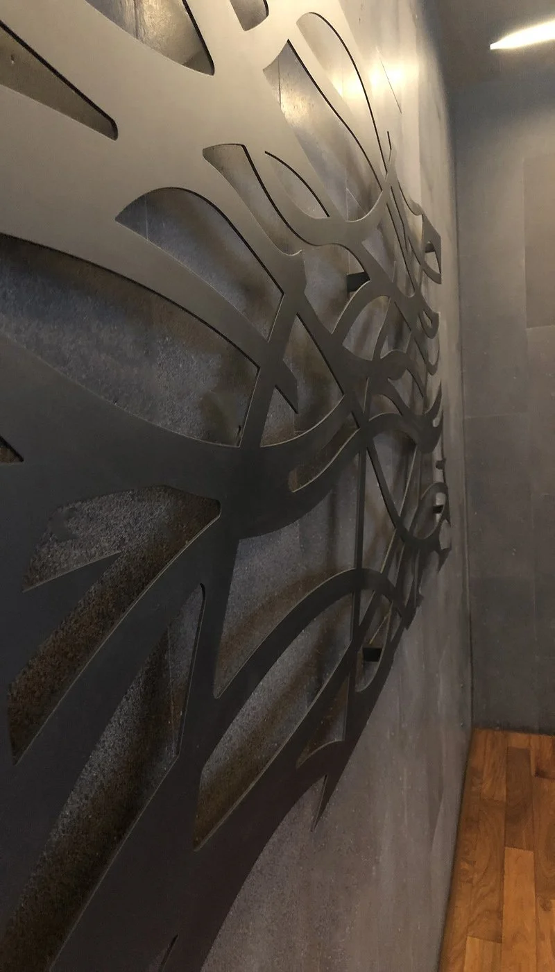 A large decorative metal wall art piece with abstract leaf-like shapes mounted on a gray wall.