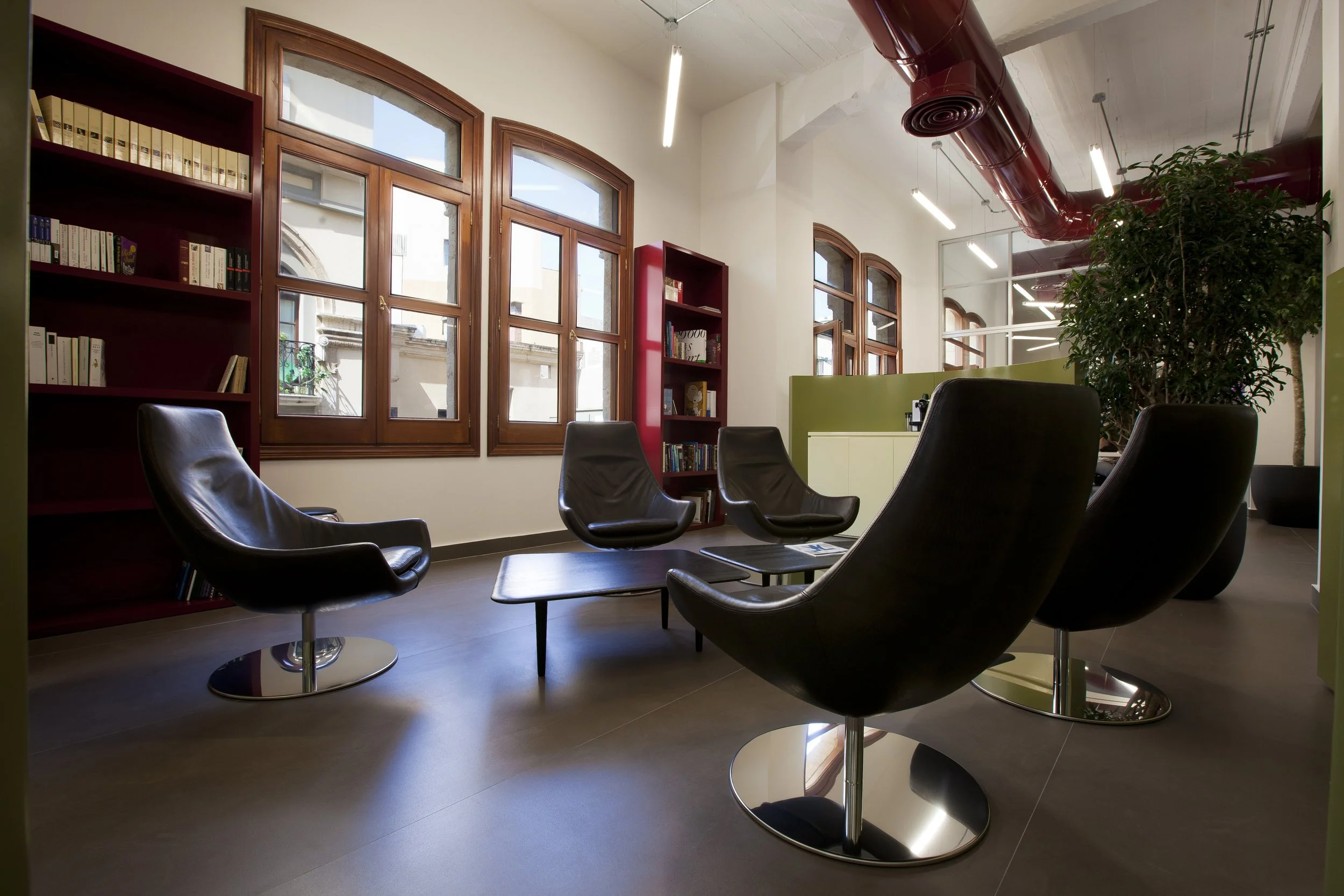 Modern lounge area with black leather chairs, wooden framed windows, and green plants.