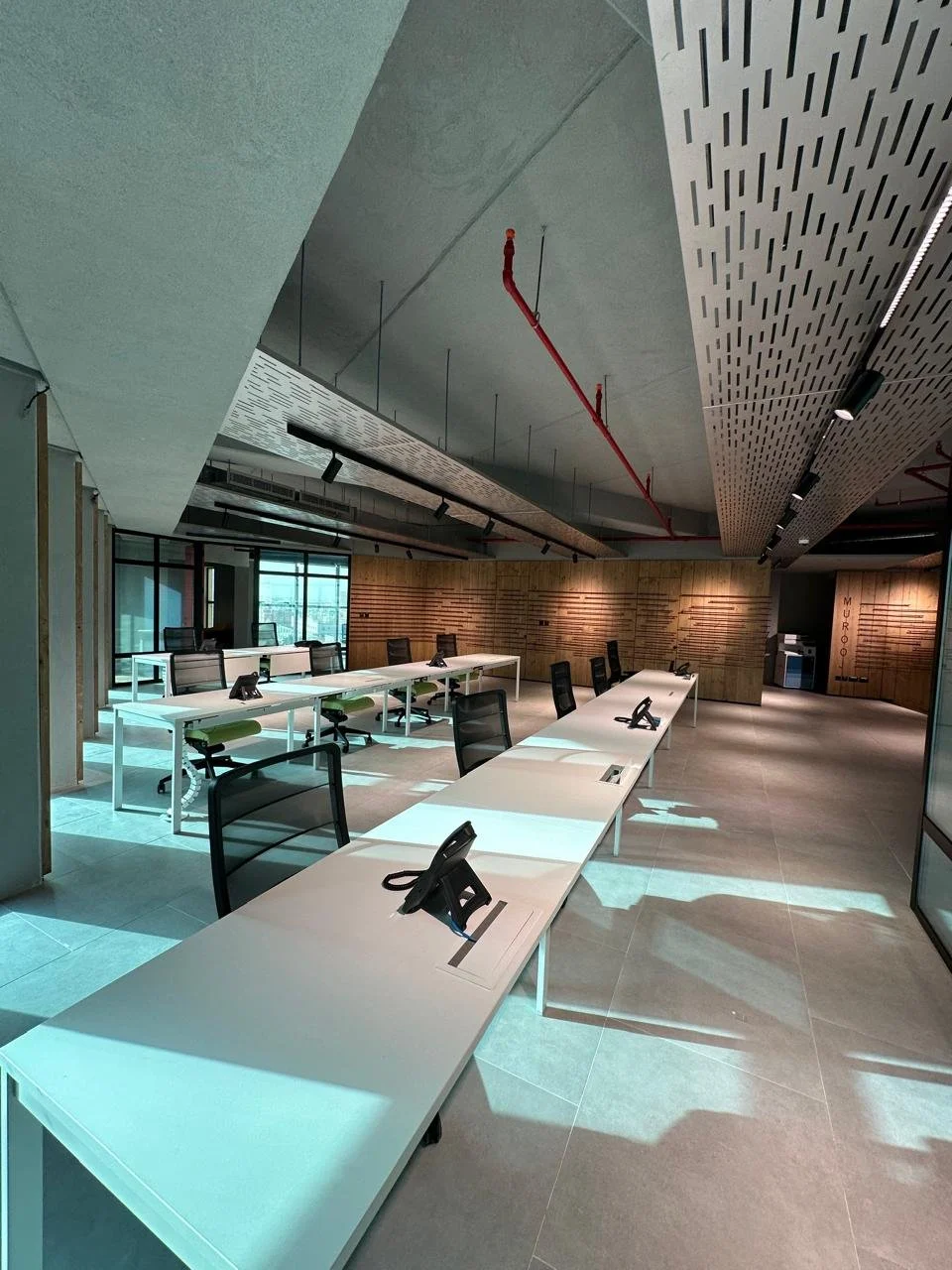 Empty modern conference room with long white tables, black office chairs, and ceiling-mounted track lighting.