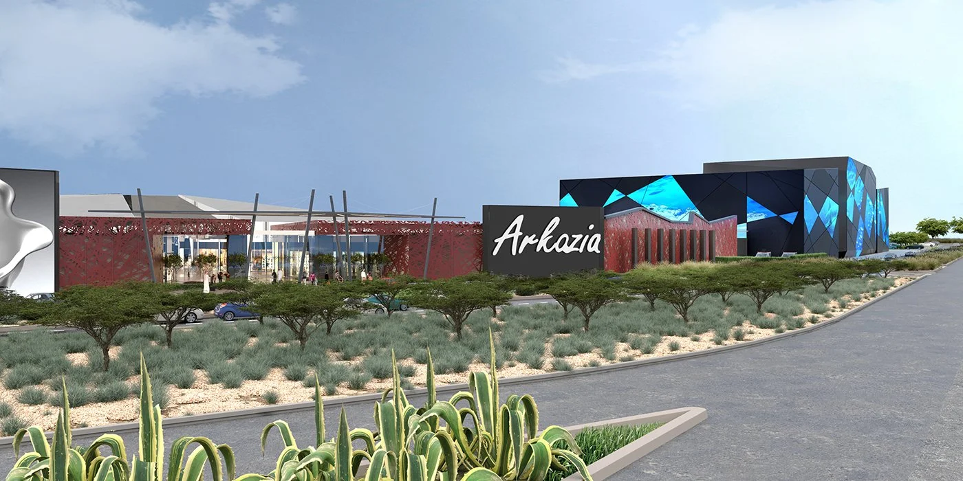 Rendering of Arkazia shopping mall with modern architecture, featuring red and black modern building designs, an entryway with large glass doors, parking lot, trees, bushes, and desert landscaping in the foreground.