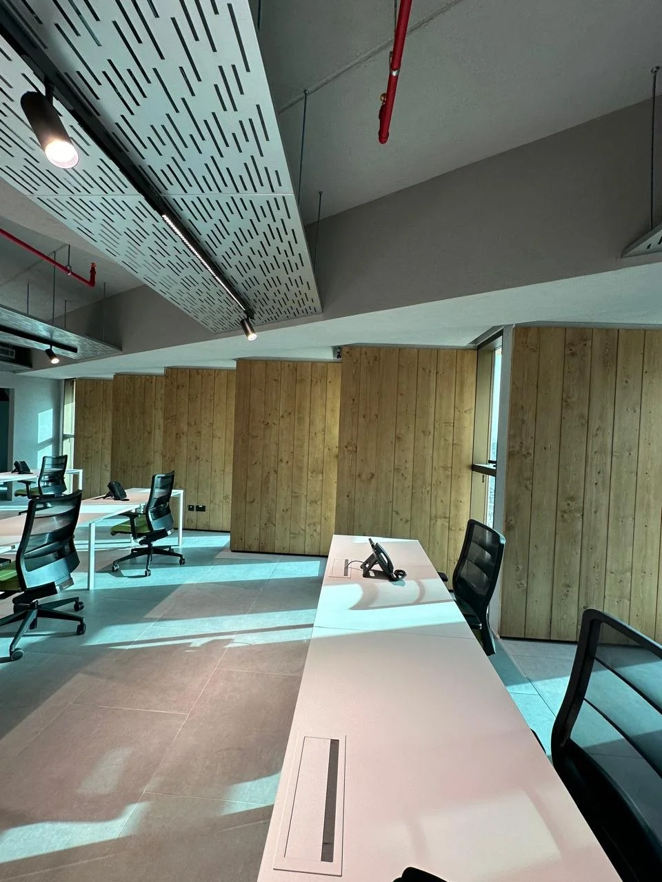 Empty modern office with desks, chairs, and telephones, illuminated by natural light from windows.