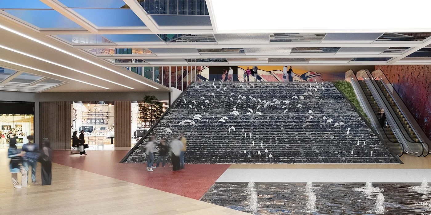 Interior of a shopping mall featuring a large staircase with water cascading down. There are escalators on the right side, and people walking around.