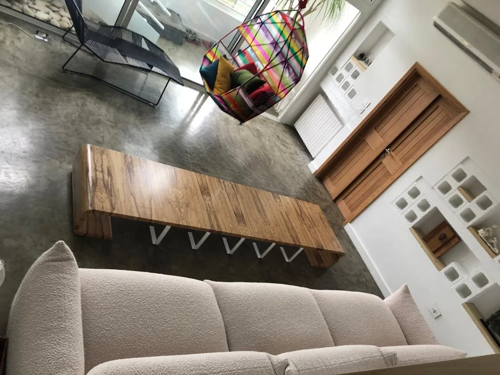 Living room with a beige sofa, a wooden bench, a colorful hanging chair with cushions, a laptop on a black metal chair, and an air conditioner on the wall.