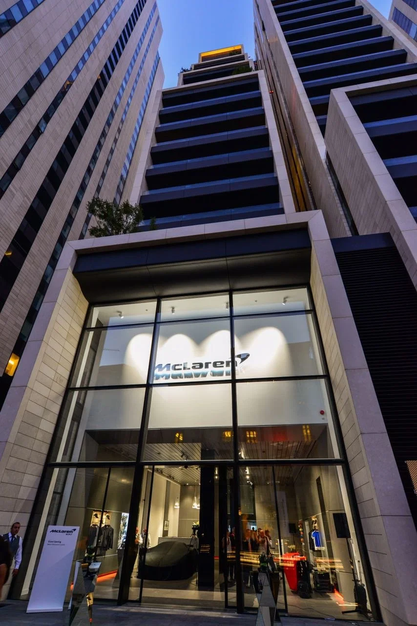 Tall modern office building with a McLaren store entrance at the ground level, glass facade, and multiple floors visible from street level.