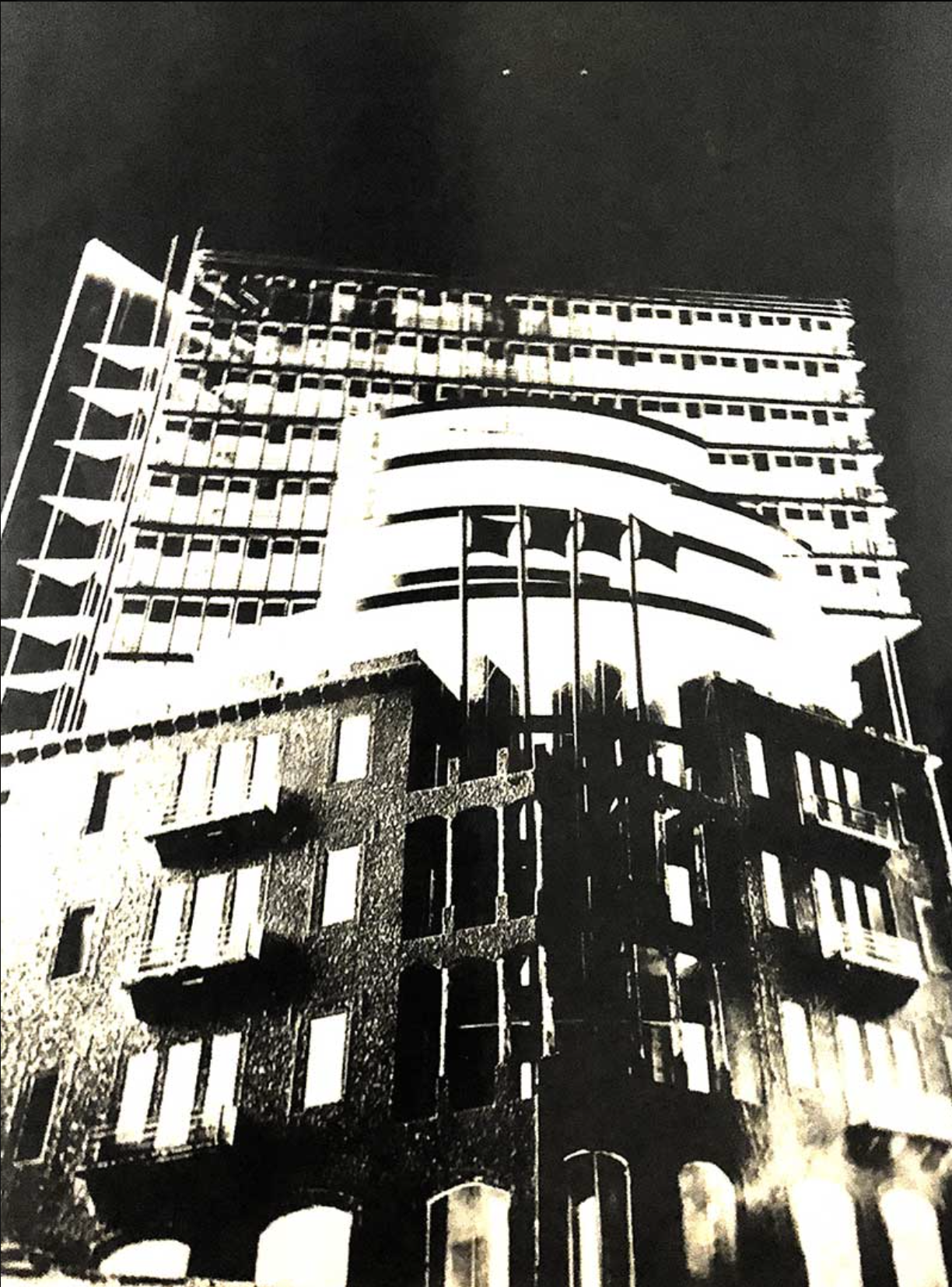 Black and white photograph of a skyscraper with unique architectural features, including curved and grid-like elements, against a dark sky.