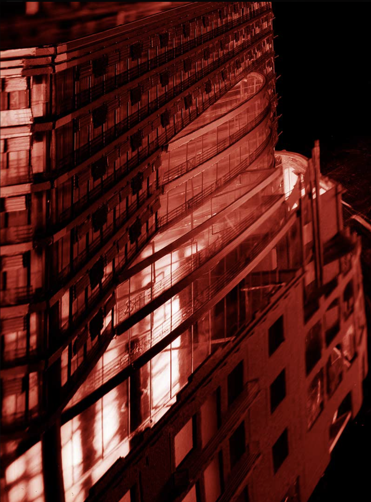 Nighttime view of a multi-story building with glass windows, illuminated with red lighting, showing balconies and the exterior structure of the building.