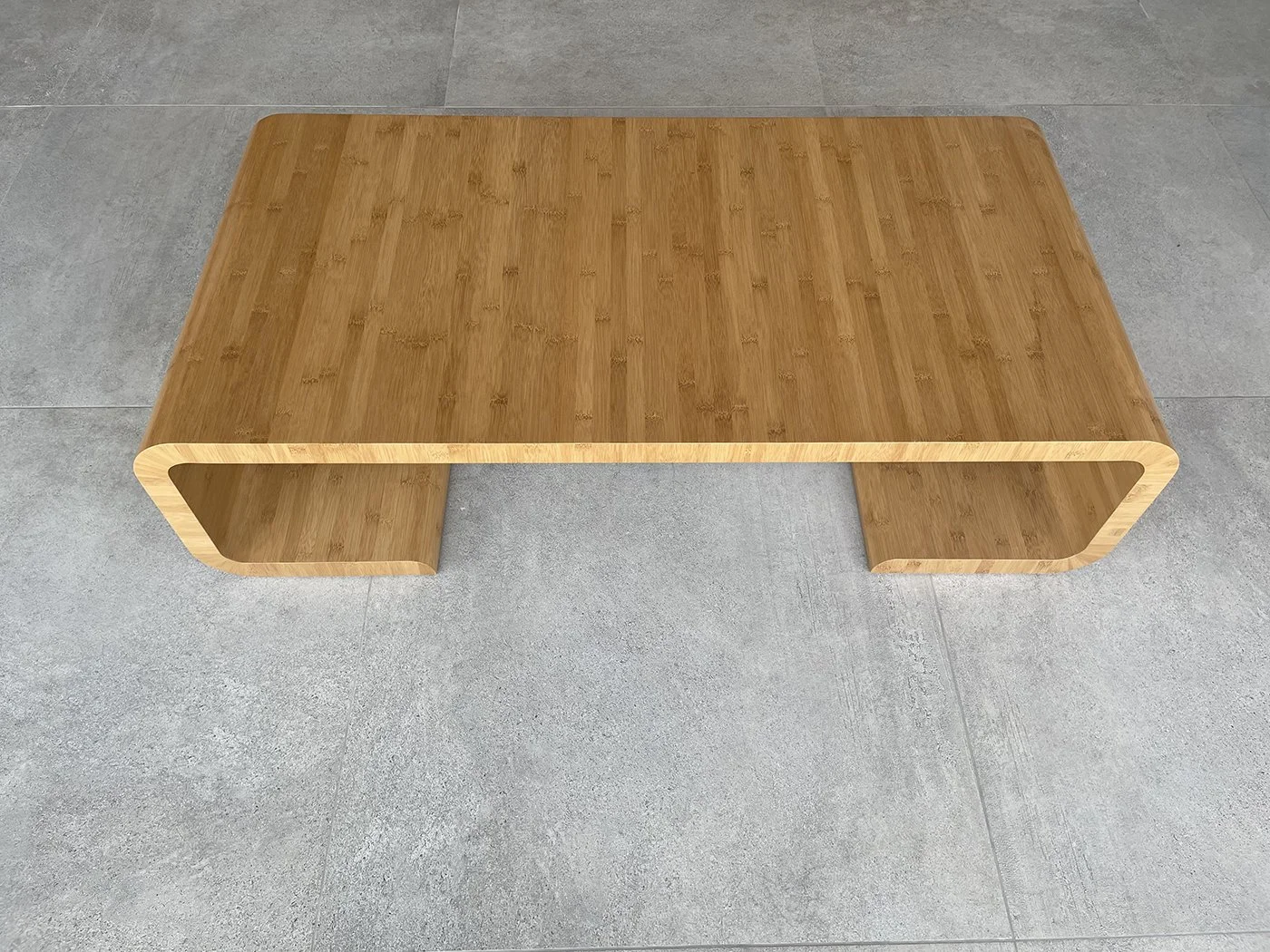 A rectangular wooden coffee table with rounded edges, placed on a gray tiled floor.