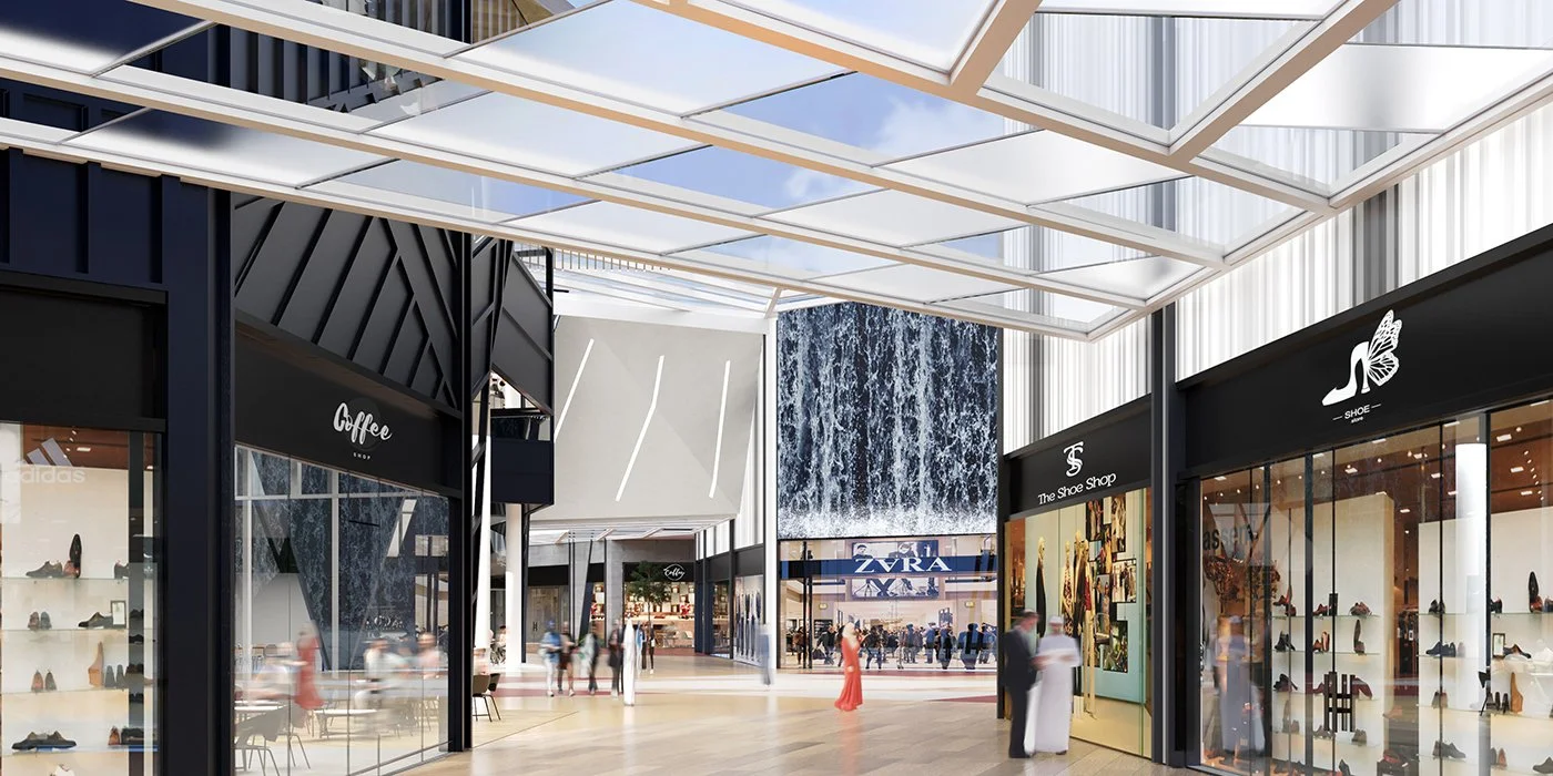 Inside a modern shopping mall with store facades, large glass windows, a waterfall display, and a decorative canopy overhead, with shoppers walking around.