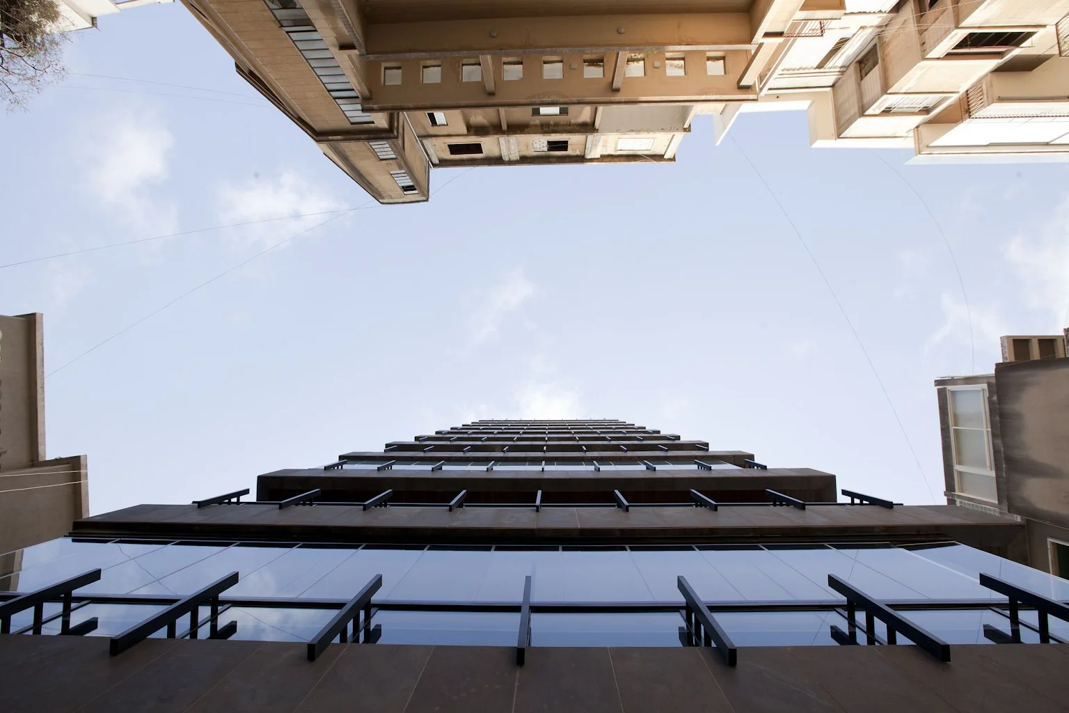 Low-angle view of tall modern residential buildings with glass windows, seen from the ground looking up towards the sky.