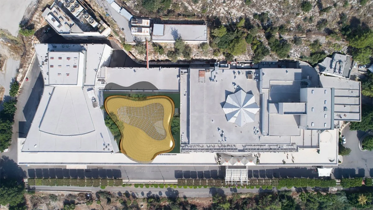 Aerial view of a building with a rooftop playground area featuring a yellow play surface and a climbing structure, surrounded by trees and nearby structures.