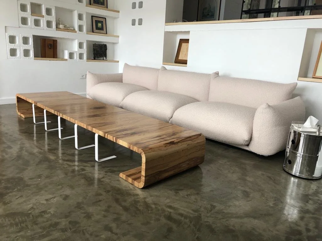 Modern living room with a large beige sofa, a wooden coffee table, and wall shelves with decorative items and framed pictures.