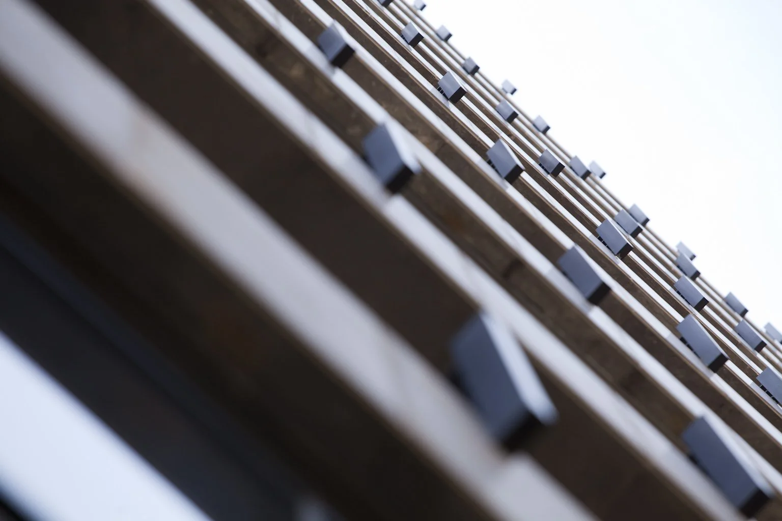 Close-up view of a modern building facade with multiple wooden slats and small rectangular lights, taken from a low angle against a bright sky.