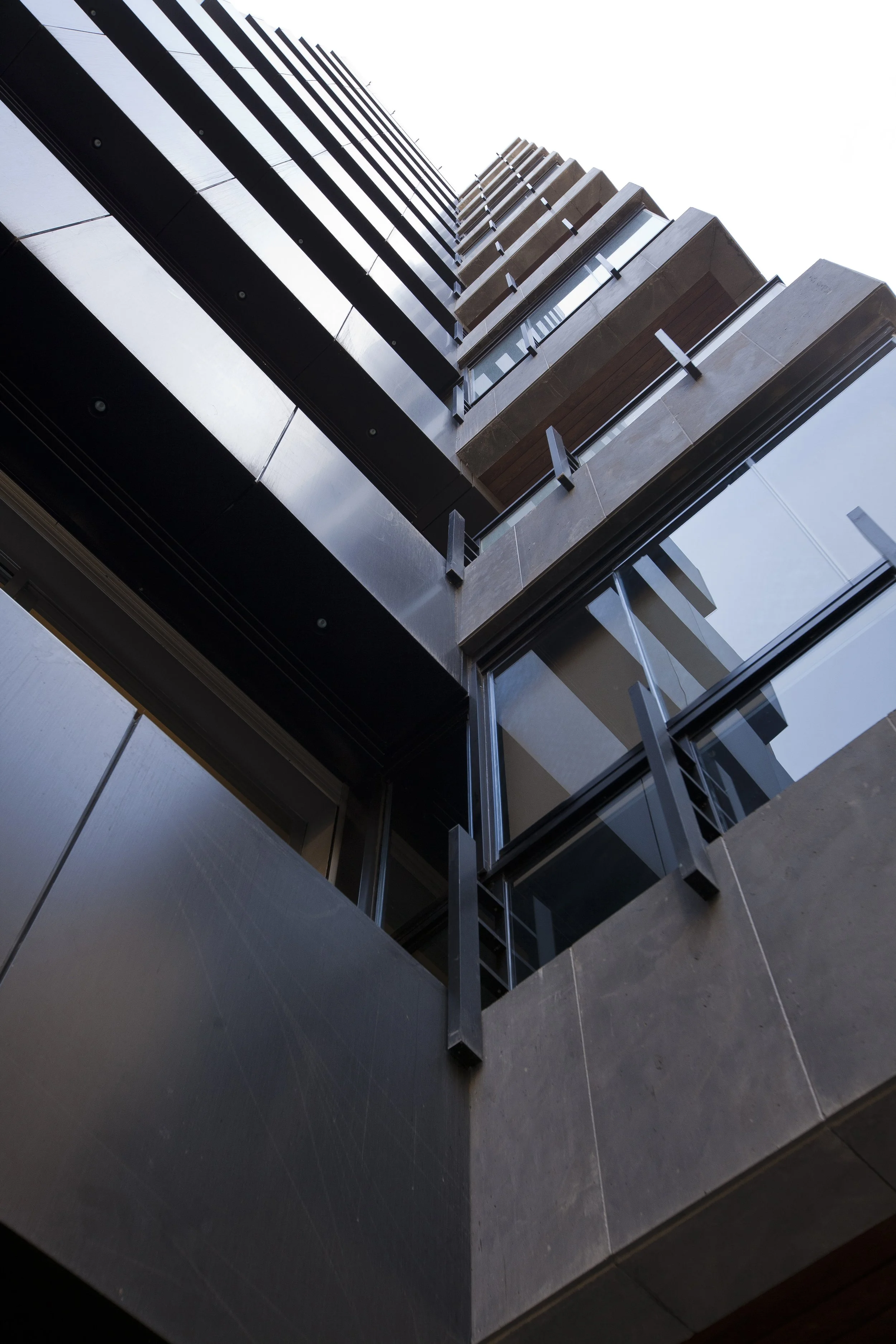 Low-angle view of a modern building with black, brown, and glass exterior panels.