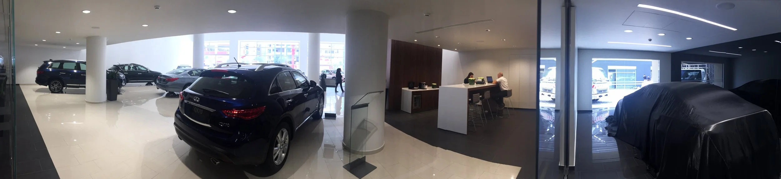 Car dealership showroom with several cars on display and a reception desk with two employees.