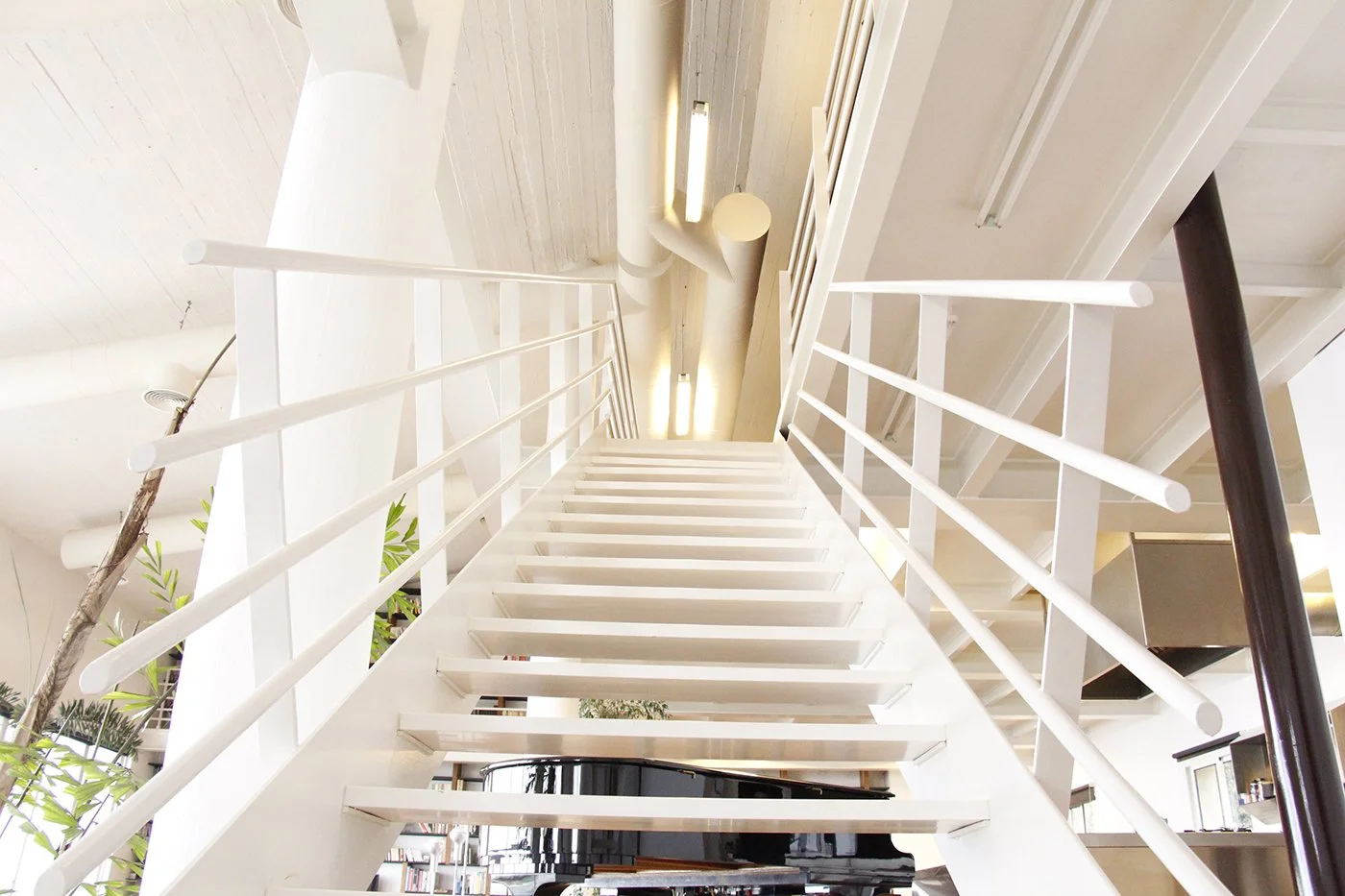 Indoor staircase with white steps and railings, viewed from below, in a modern building with wooden ceiling and lighting.
