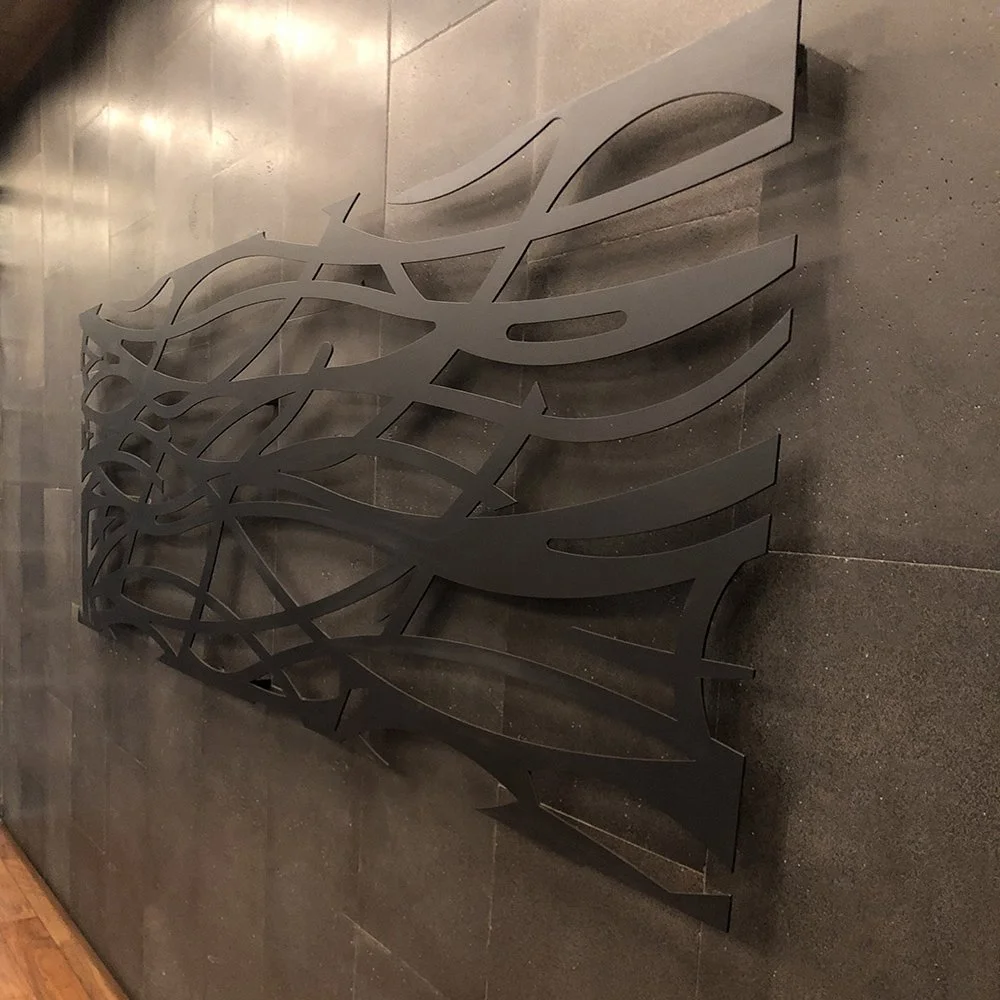 Decorative black metal wall art with an abstract, flowing design mounted on a gray tiled wall.