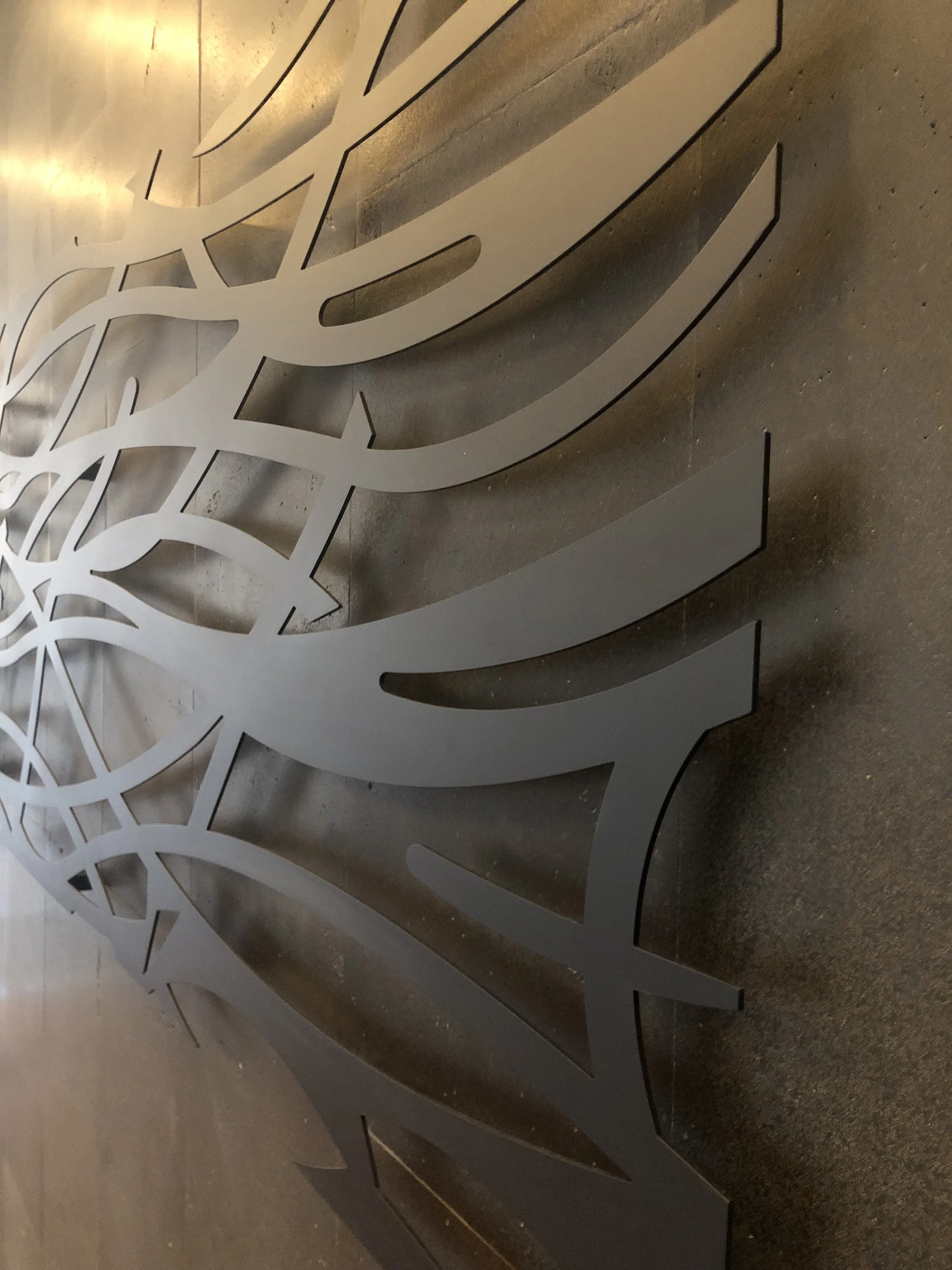 Close-up of a decorative metal wall art piece with intricate swirling and floral patterns, mounted on a textured wall.