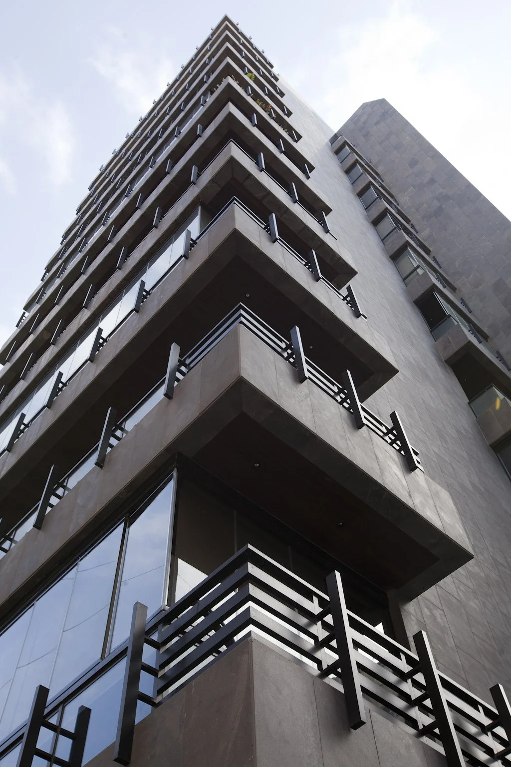 Low-angle view of a modern high-rise building with glass windows and balconies, taken against a partly cloudy sky.