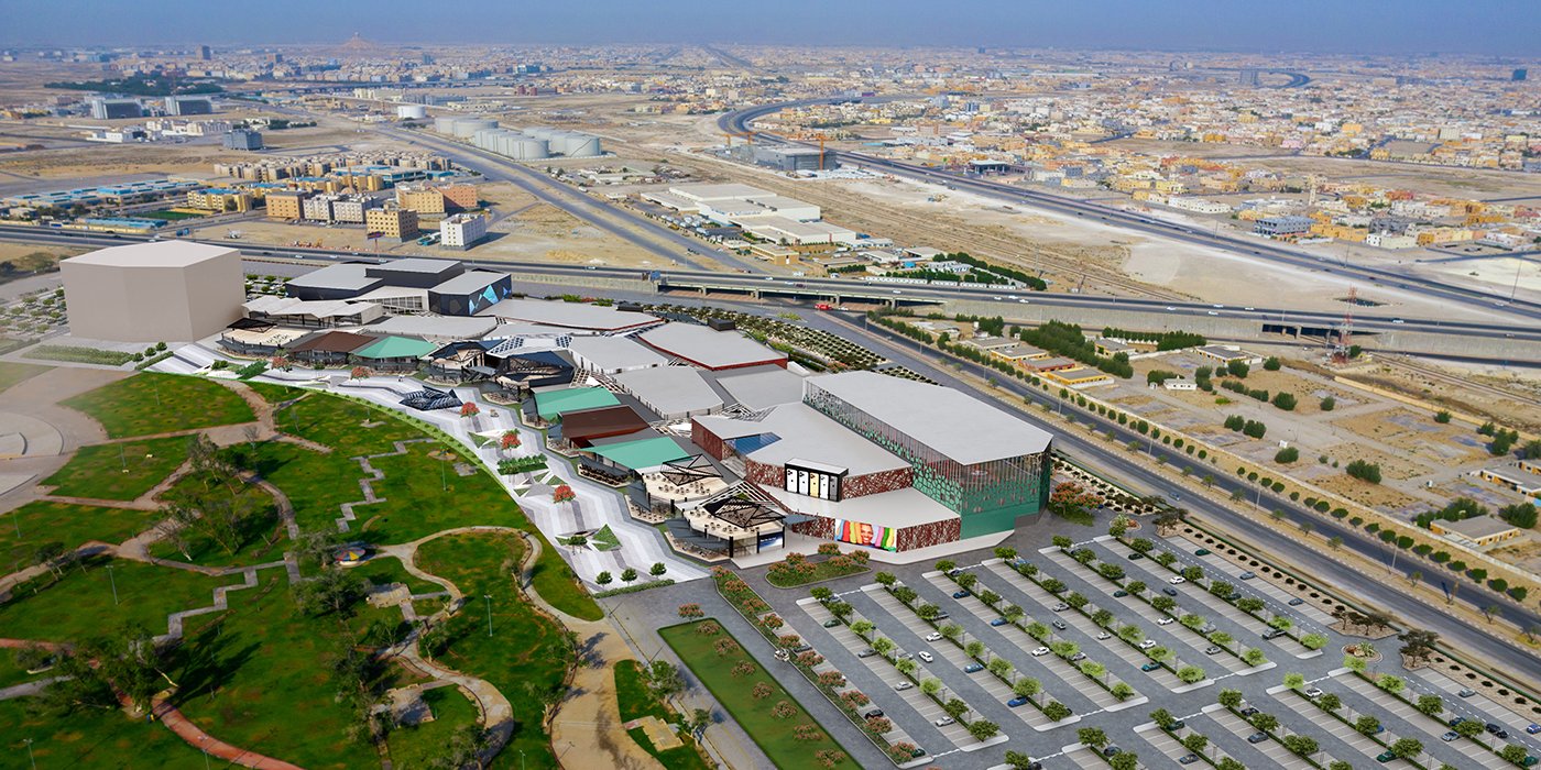 Aerial view of a large shopping mall with parking lots, cityscape, and highways in the background.