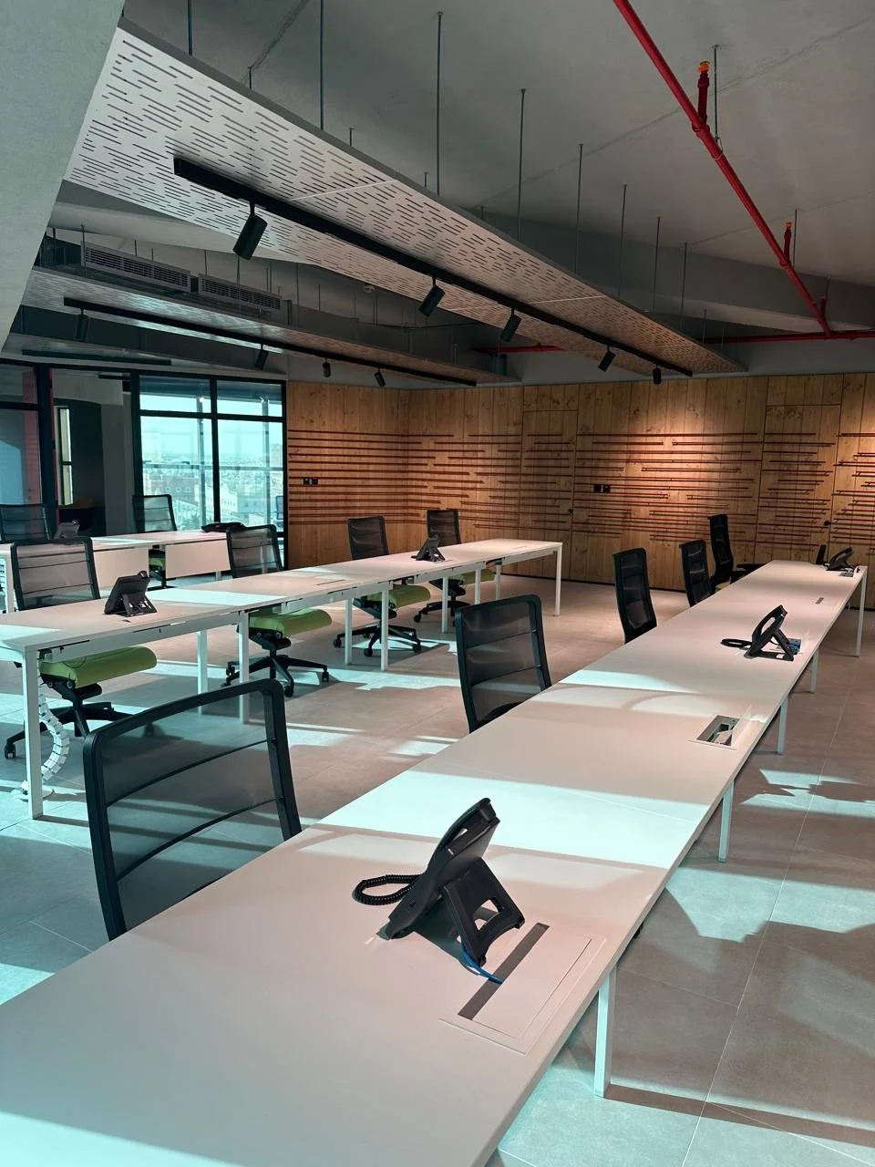 Empty conference room with white tables, black office chairs, and telephones, with wood-paneled walls and large windows providing natural light.