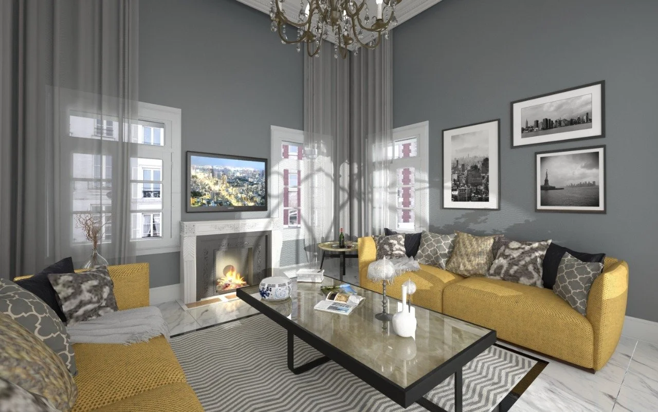 Living room with gray walls, white window frames, and black and white framed photographs on the wall. There are two yellow sofas with patterned throw pillows, a marble top coffee table, and a fireplace with a television above. Sunlight filters throug