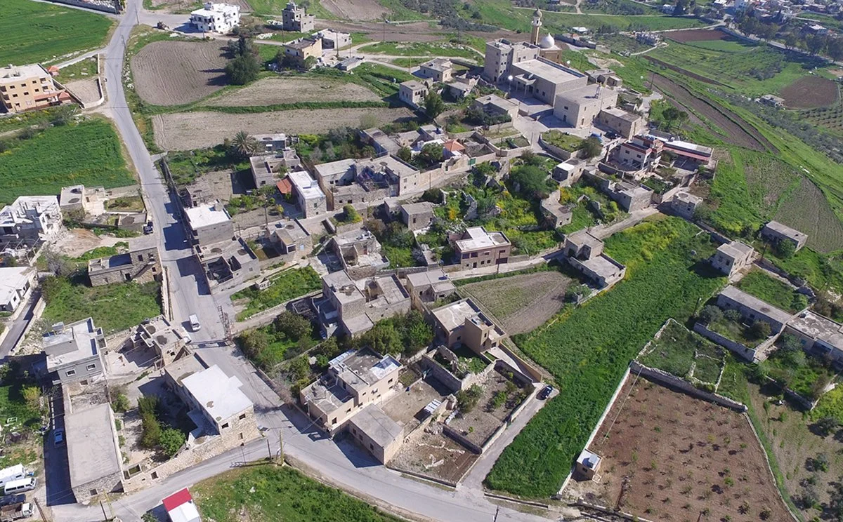 Aerial view of a rural village with stone buildings, roads, and surrounding agricultural fields.