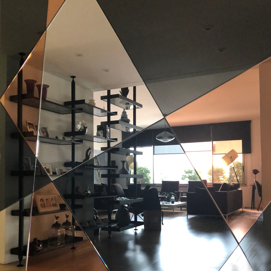 Reflection of a modern living room with shelves, sofas, and a large window, seen through a diamond-shaped mirror.