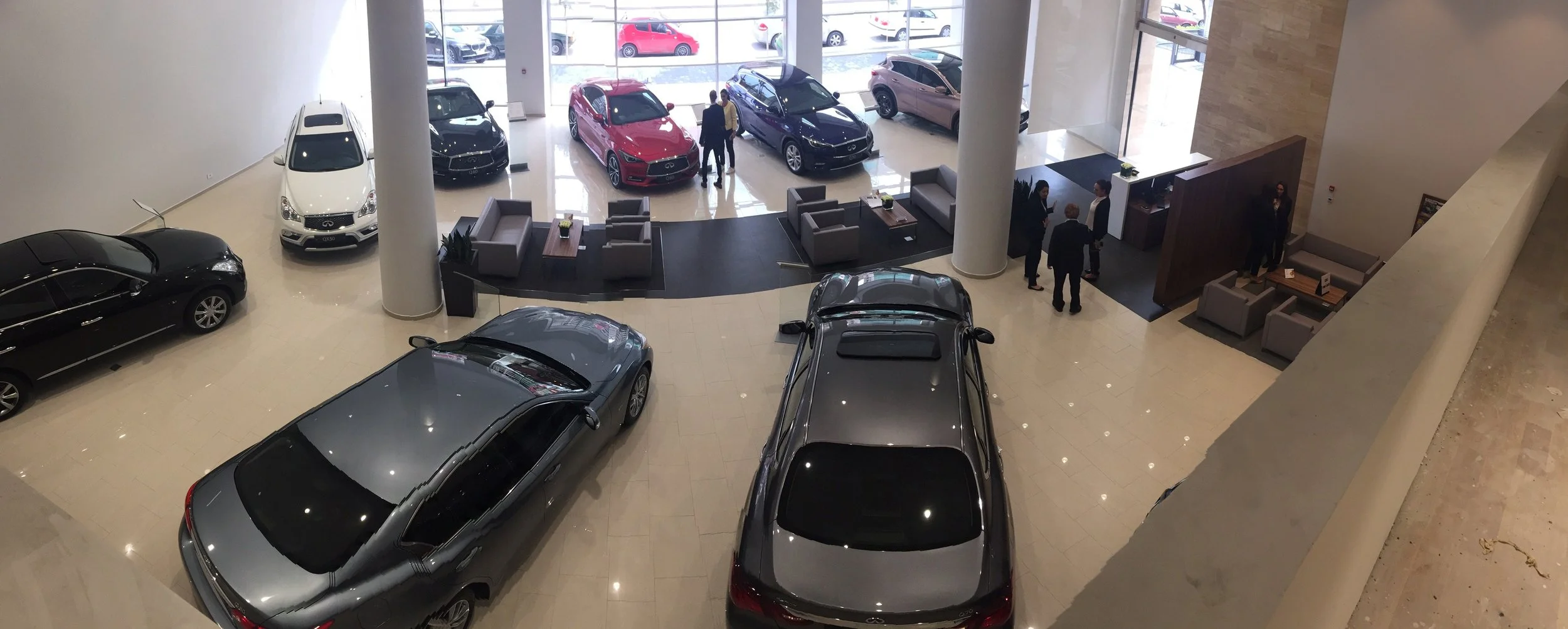 Interior view of a car dealership showroom with several new cars on display, a seating area, and people talking.