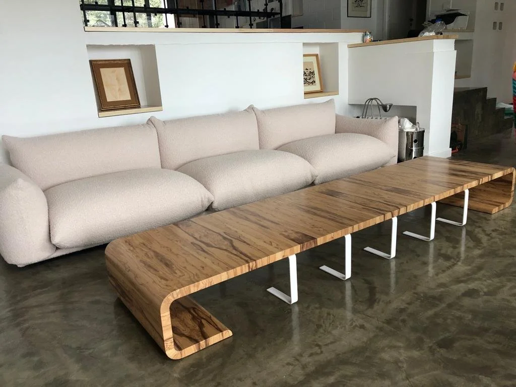 Modern living room with a large beige sofa and a long wooden coffee table with a curved design and metal supports.