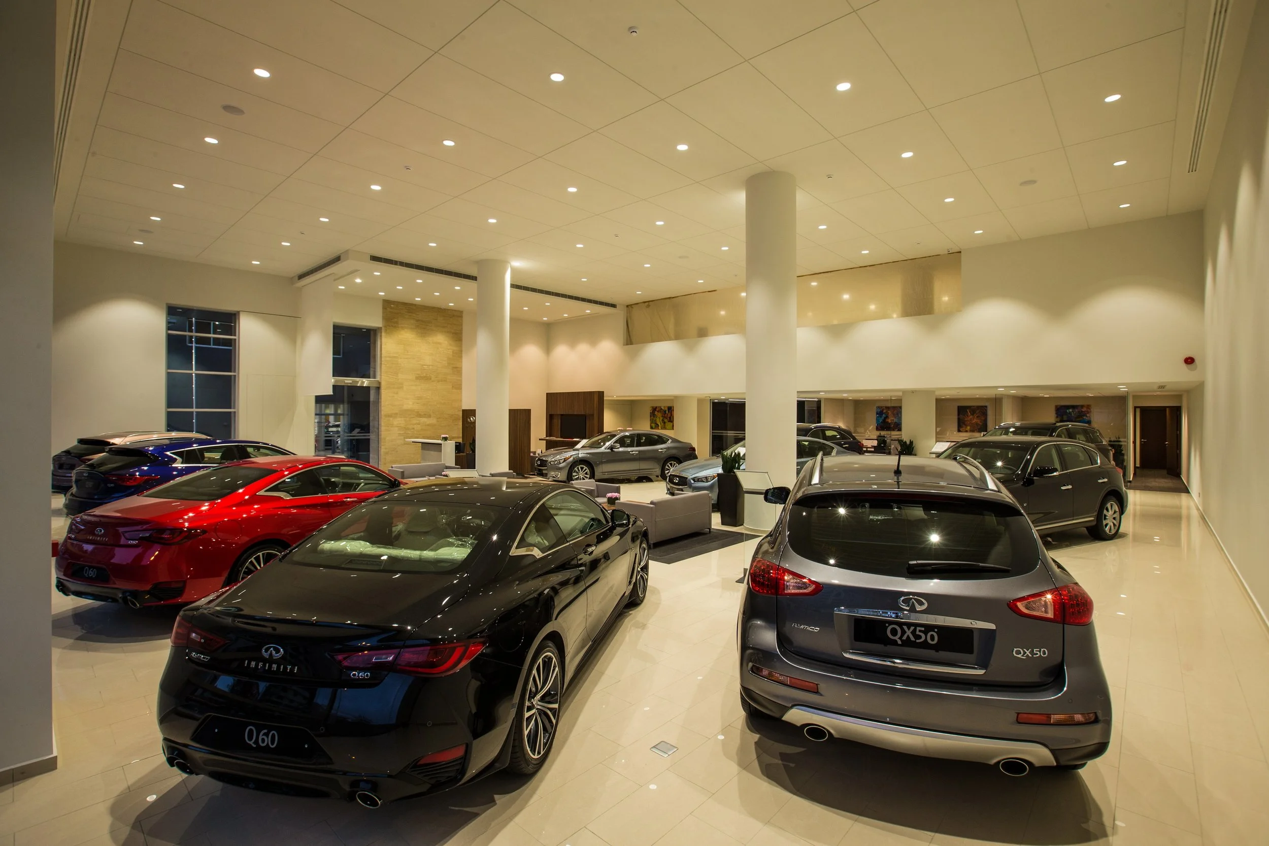 An indoor car showroom displaying multiple luxury cars, including models from Infiniti and QX series, under bright ceiling lighting with a modern, spacious interior design.