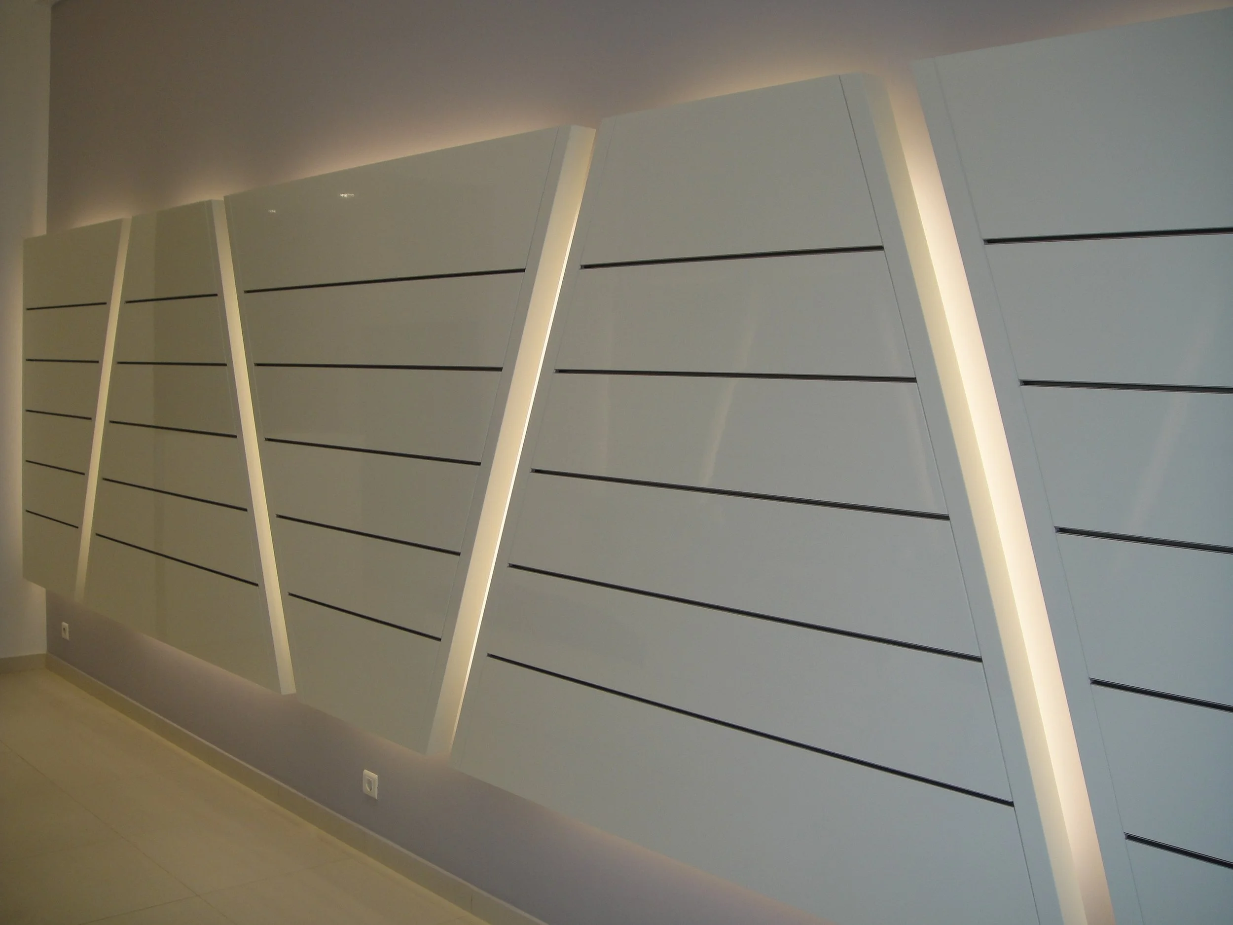 Modern interior wall with beige and white color scheme, featuring angled white panels with black horizontal lines, illuminated by soft lighting.