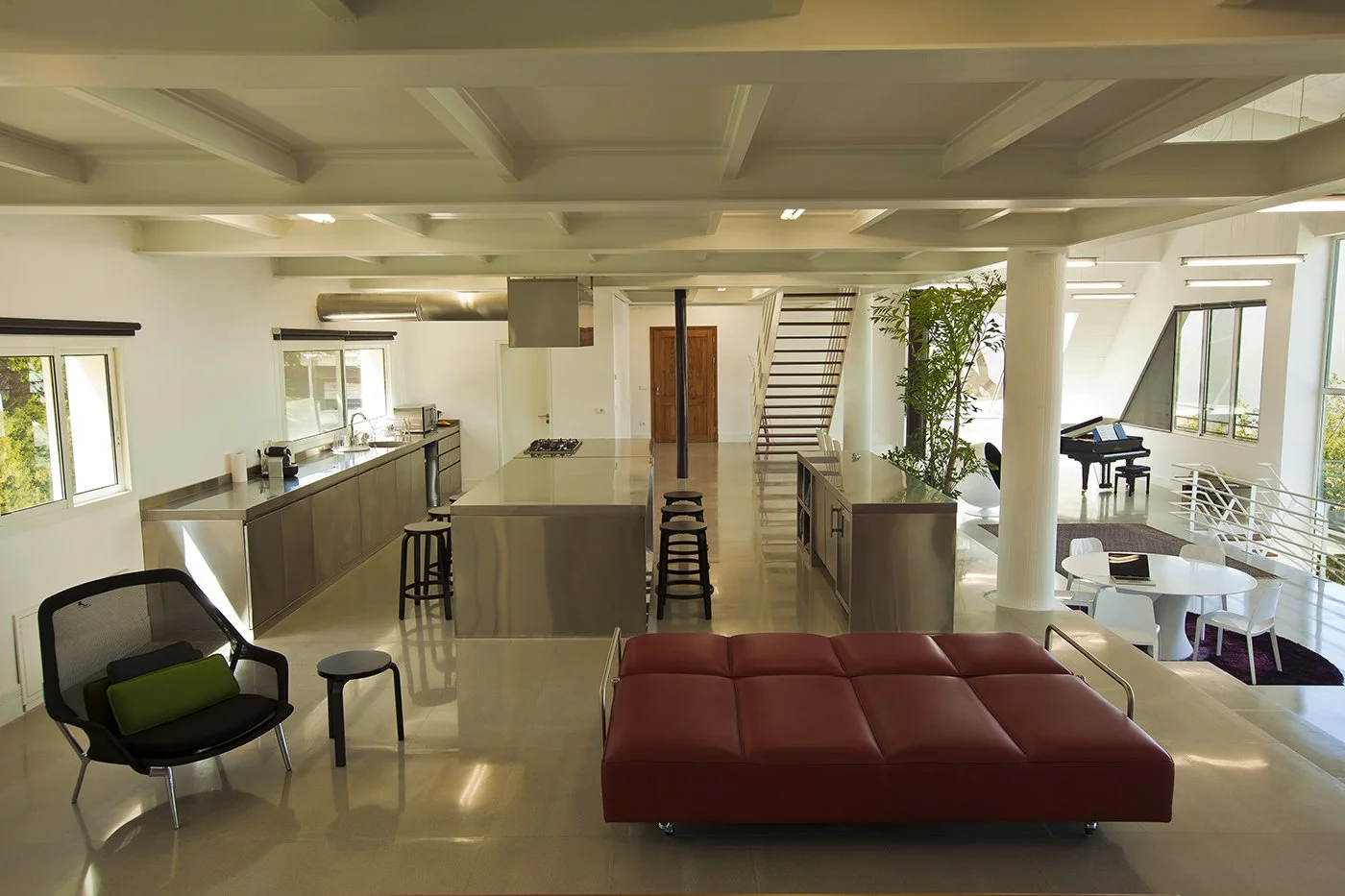 Open-concept modern living space with a kitchen, dining area, and piano, featuring large windows, minimalist design, and natural light.