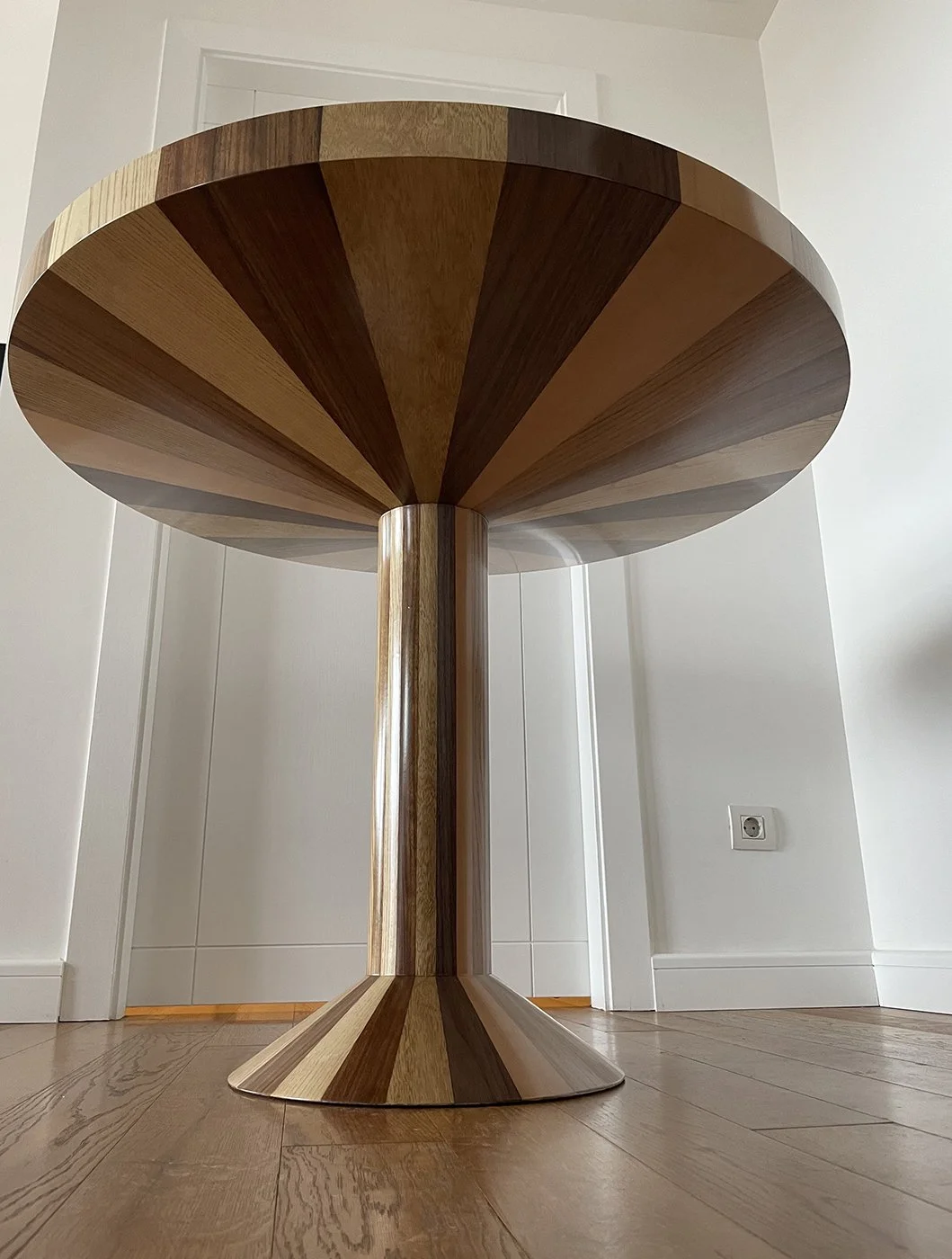 A wooden table with a conical base and a rounded top, made from striped wood in different shades.