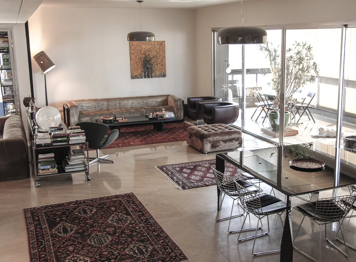 Living room with a large sofa, black armchairs, a glass dining table with four chairs, and an outdoor balcony with a table and four chairs.