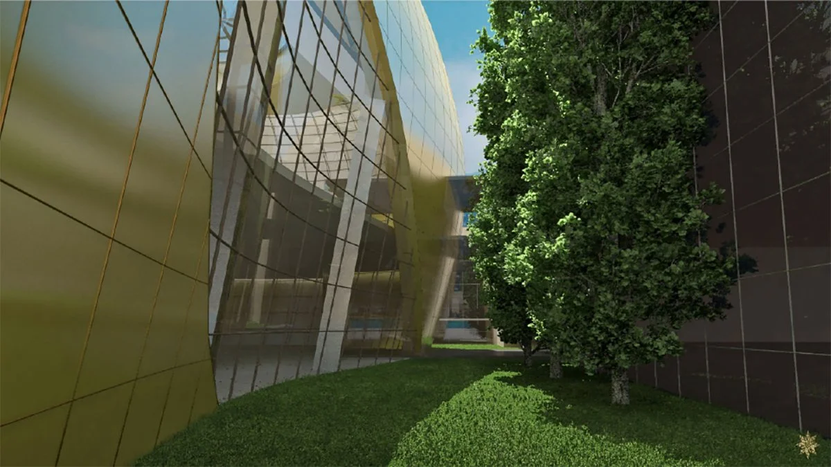 Modern glass building with reflecting surfaces, surrounded by green trees and grass.