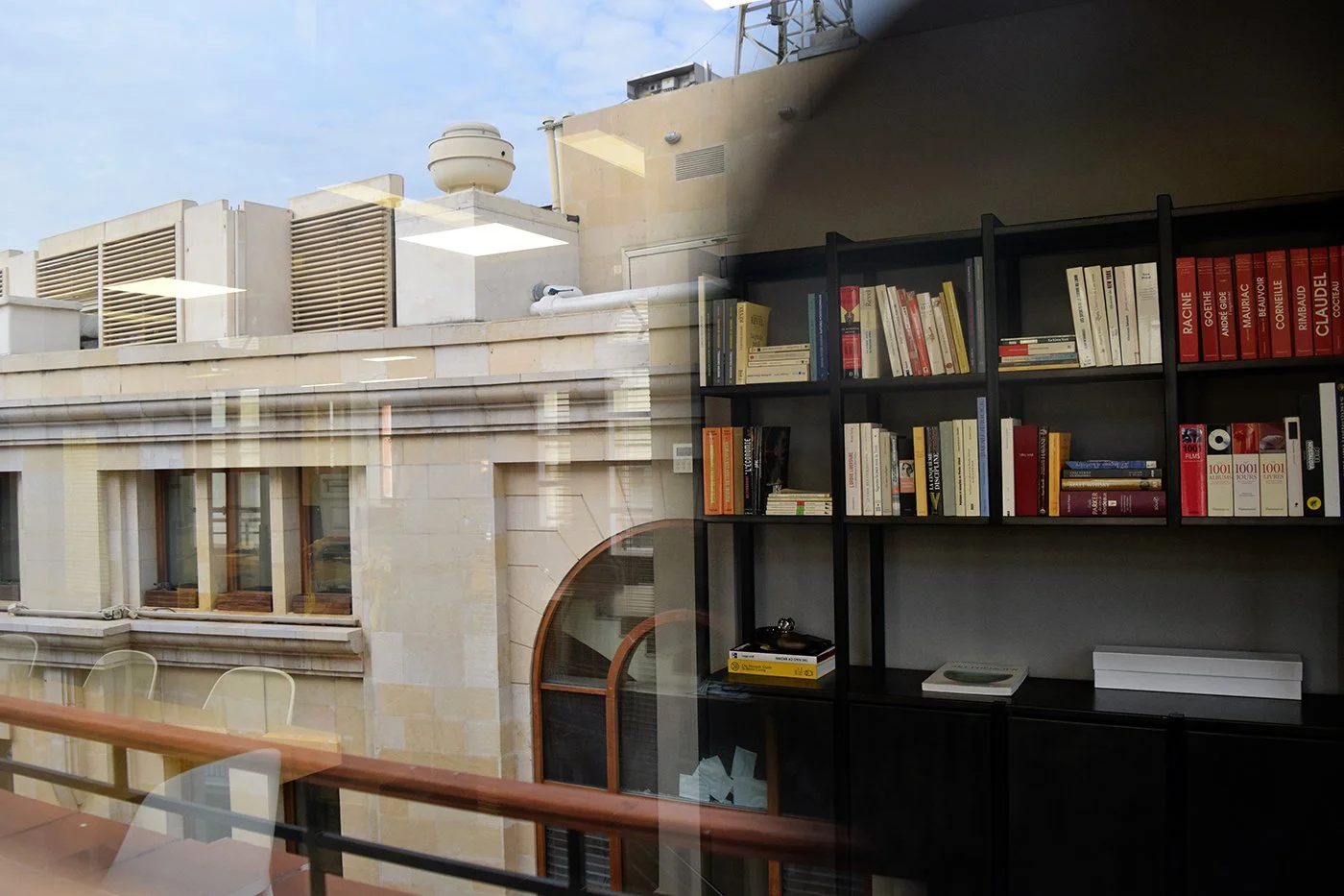 Reflection of a building and bookshelves seen through a glass window.