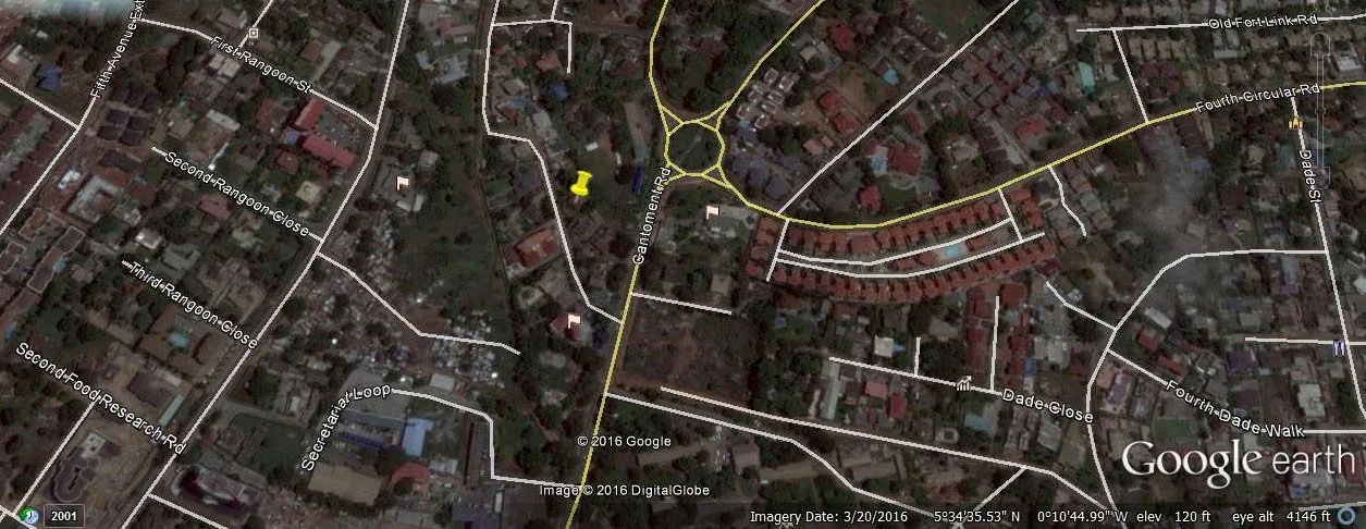 Satellite map view of a suburban neighborhood showing streets, houses, and a roundabout. Isolated areas with trees and residential structures are visible.