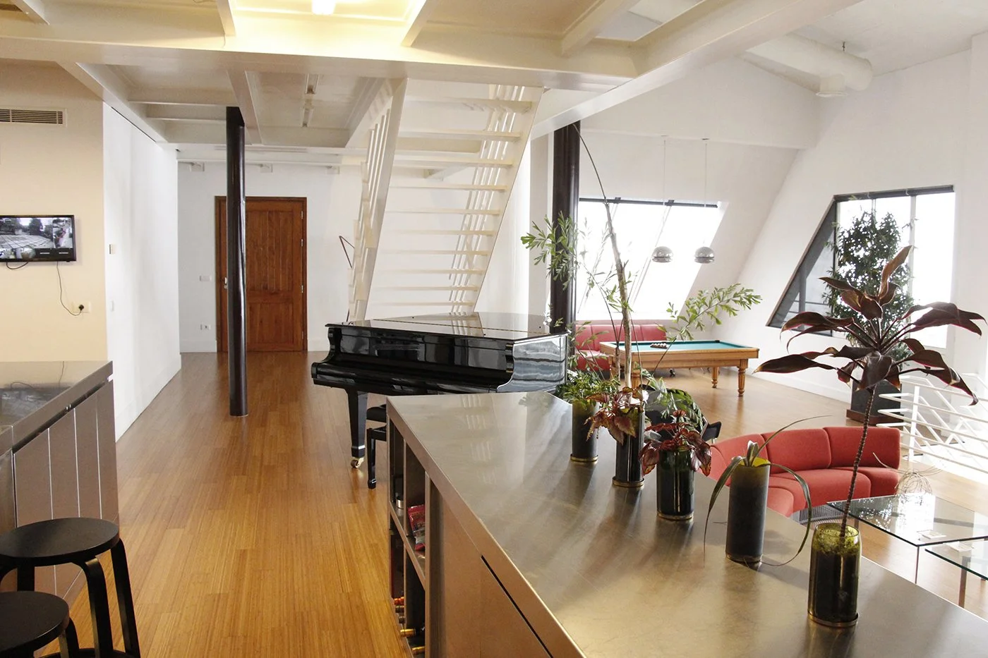 Modern open-concept living space with a black grand piano, a pool table, vibrant orange seating, plants, and large windows