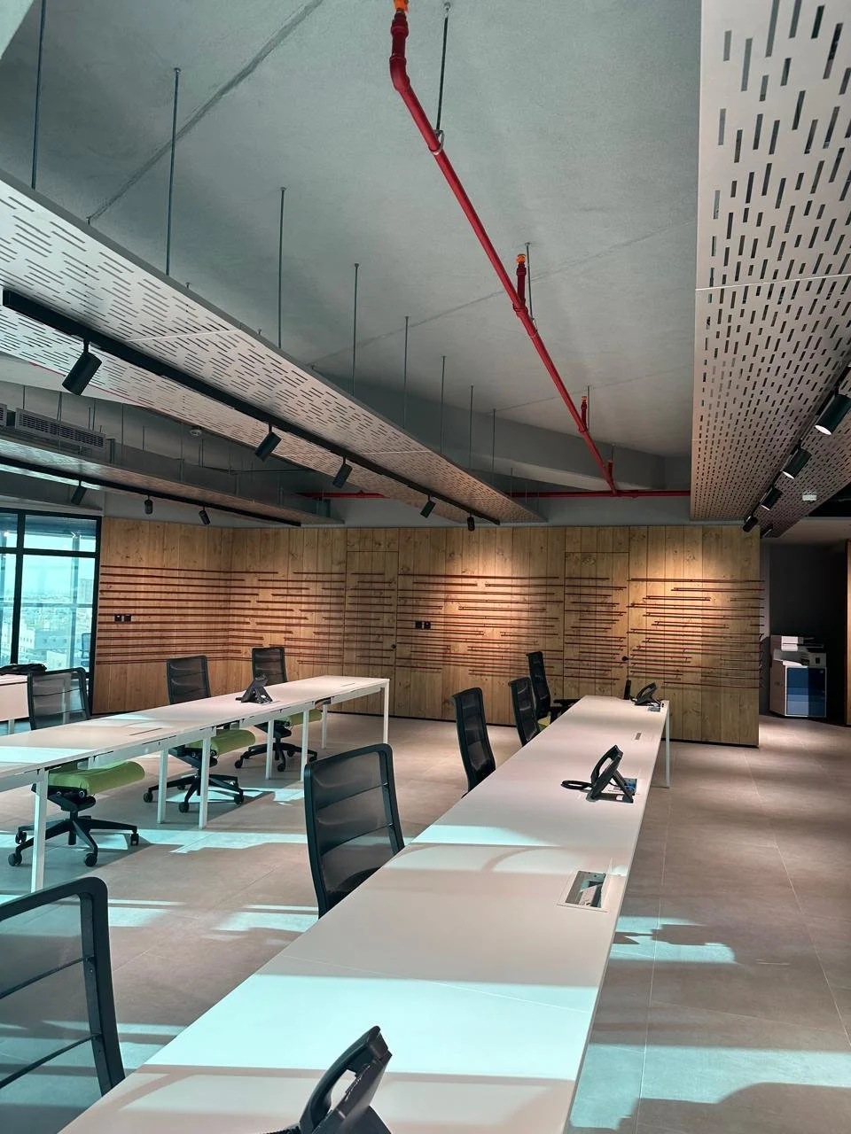 Empty modern conference room with white tables, black chairs, wood-paneled wall, and ceiling-mounted lighting