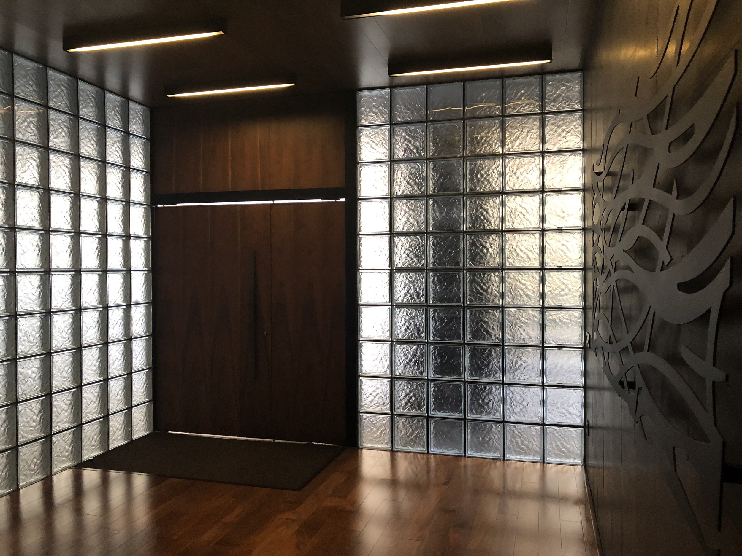 Lobby area with glass block walls, wooden door, and intricate design on the right wall